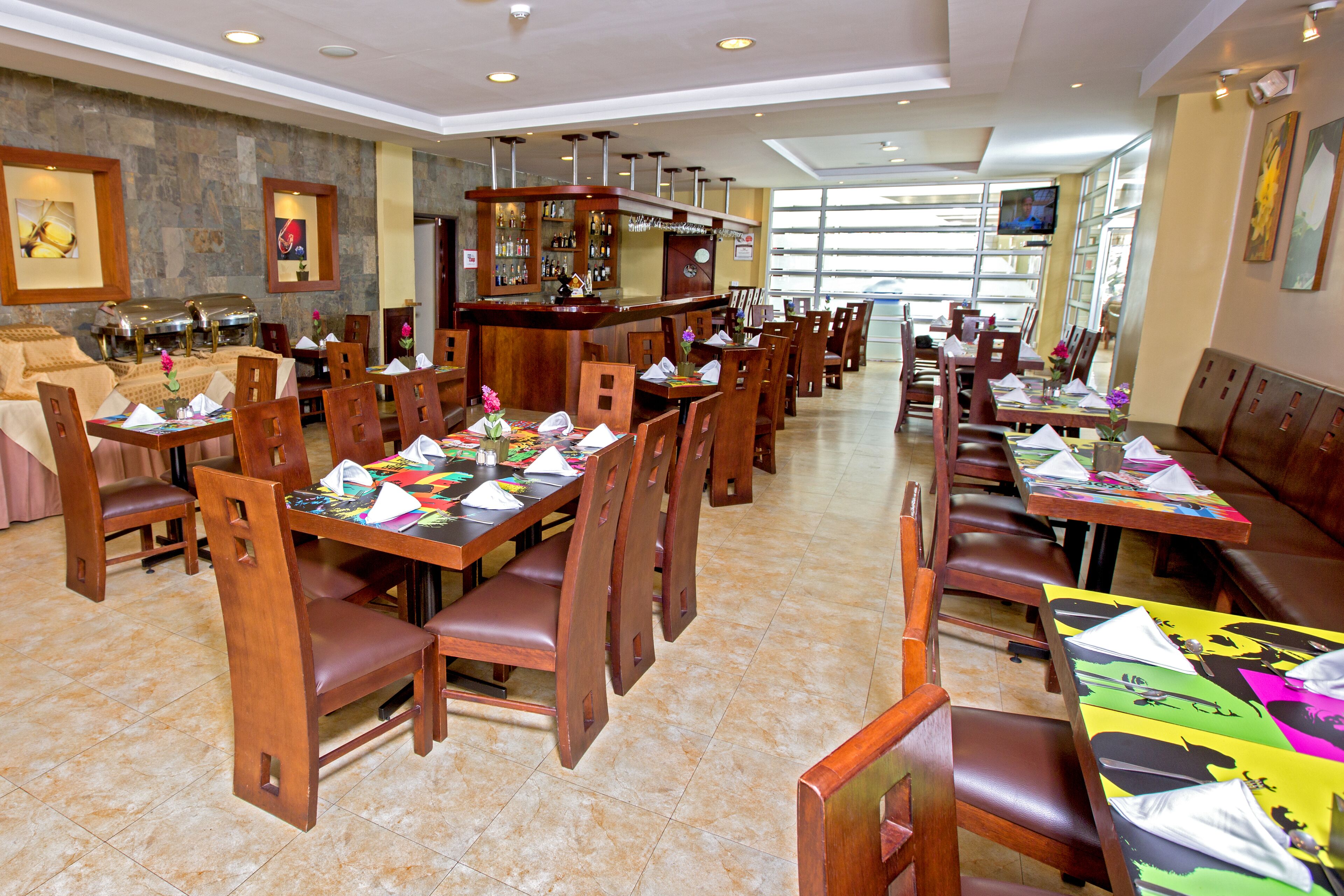 A restaurant with multiple dining tables and booths, a bar area, and a television screen.