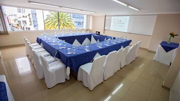 A conference room with a long table set for a meeting, white chairs, and a projector screen.
