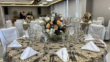 Een balzaal met ronde tafels gedekt voor een formeel evenement, met bloemstukken als middelpunt en witte tafelkleden.