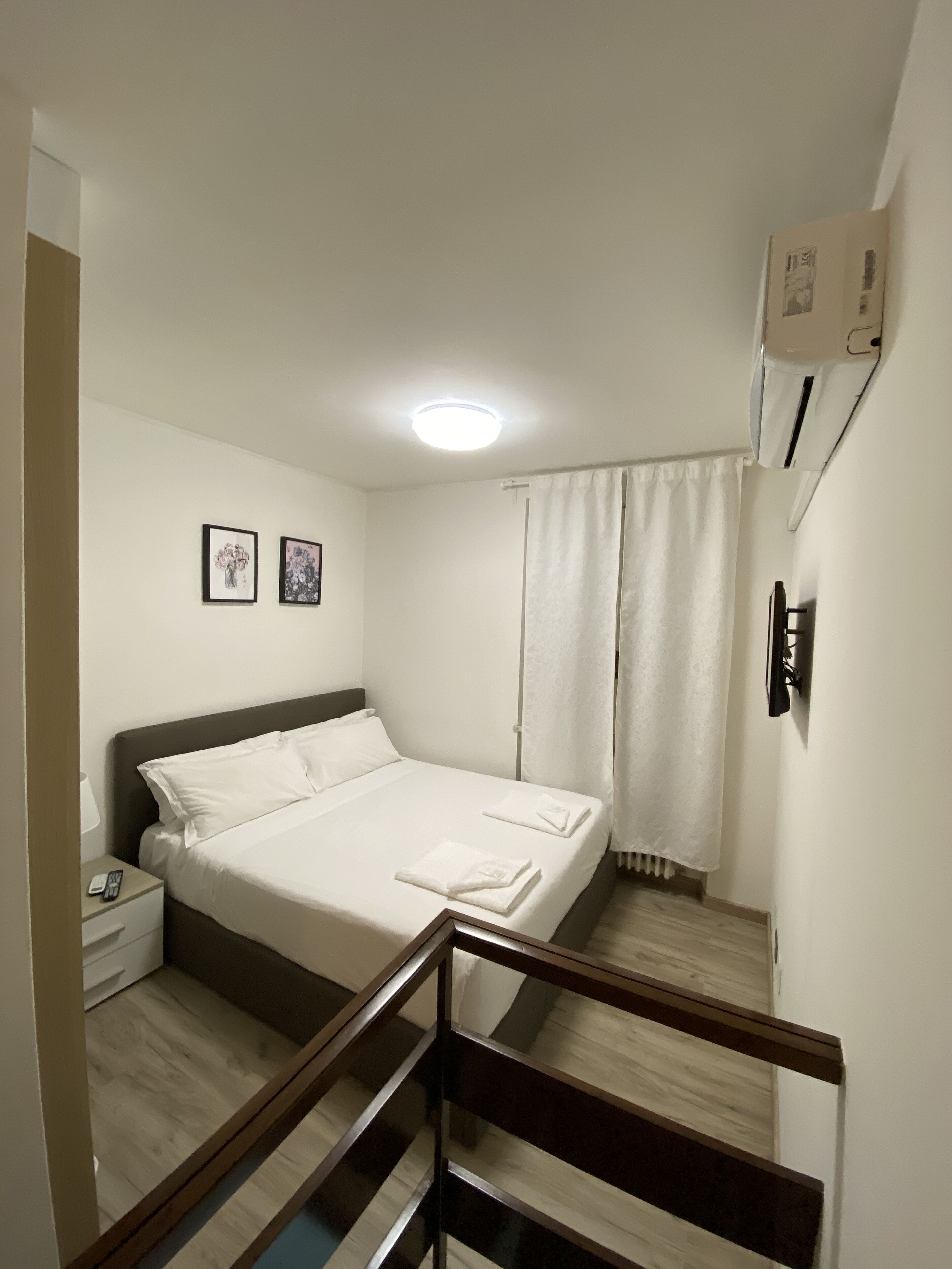 A hotel room with a bed, a nightstand, a lamp, a framed picture, and a window with curtains.