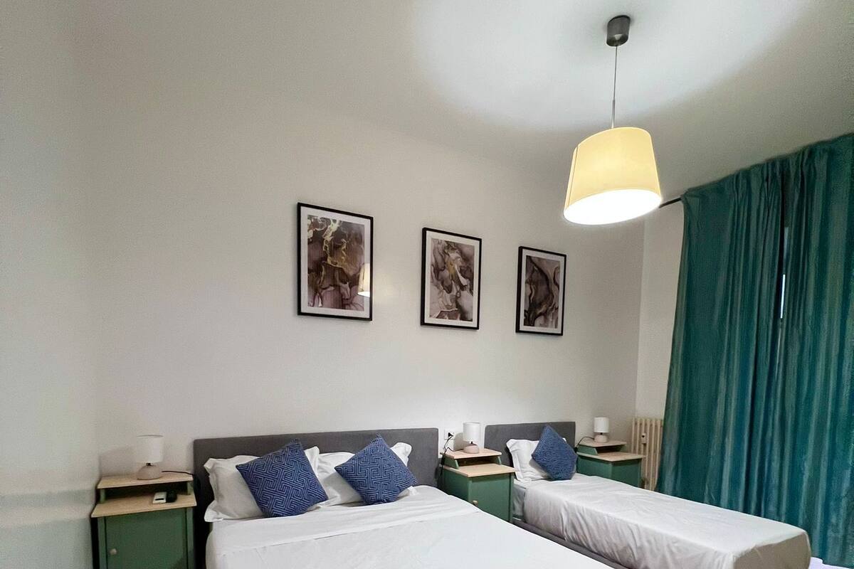 A double room with two beds, a ceiling light, and three framed pictures on the wall.