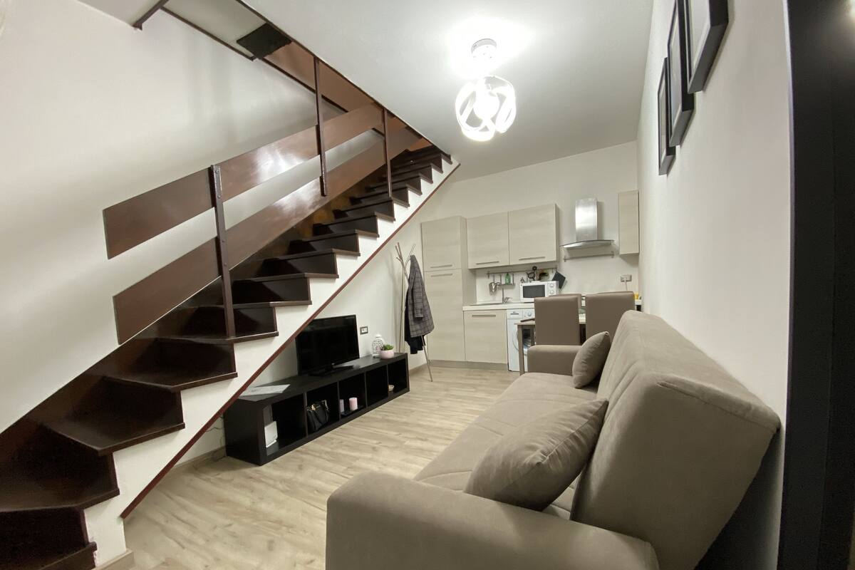 A modern apartment with a staircase, a living room with a sofa, and a kitchen area.