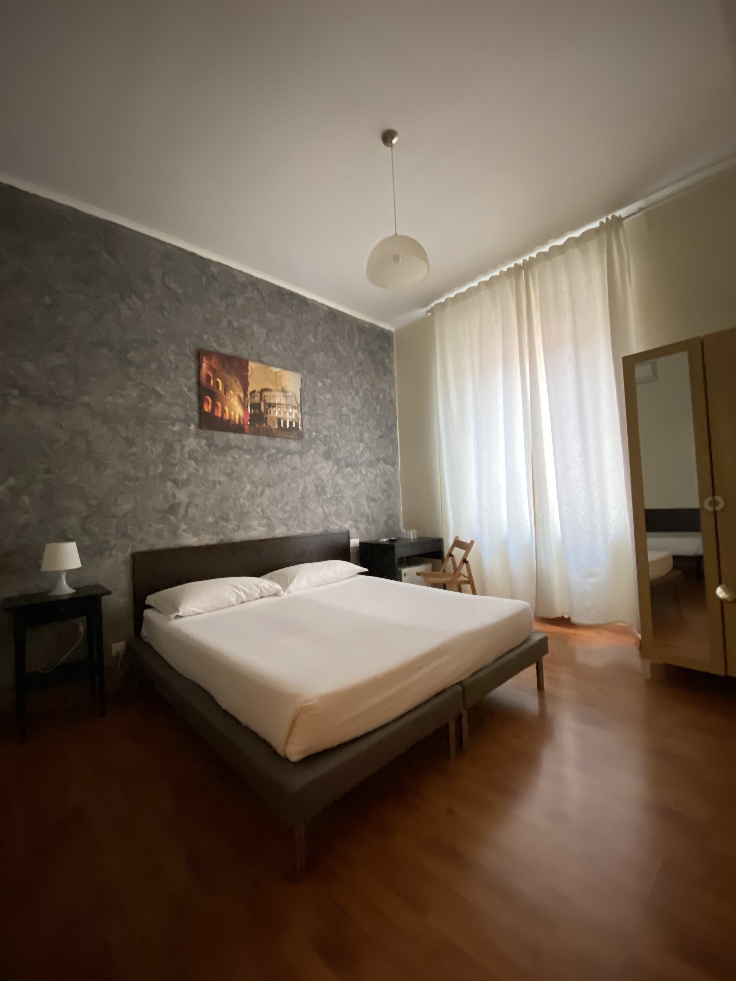 Ein Schlafzimmer mit einem großen Bett, einem Nachttisch, einer Lampe, einem Bild an der Wand und einem Kleiderschrank.