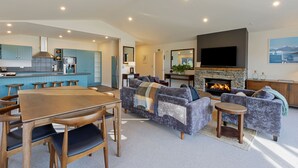 A modern living room with a fireplace, a dining area, and a kitchen with blue cabinets. - Queenstown House (Queenstown)