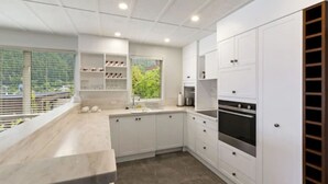 A modern kitchen with white cabinetry, a built-in oven, and a large window overlooking greenery. - Queenstown House (Queenstown)