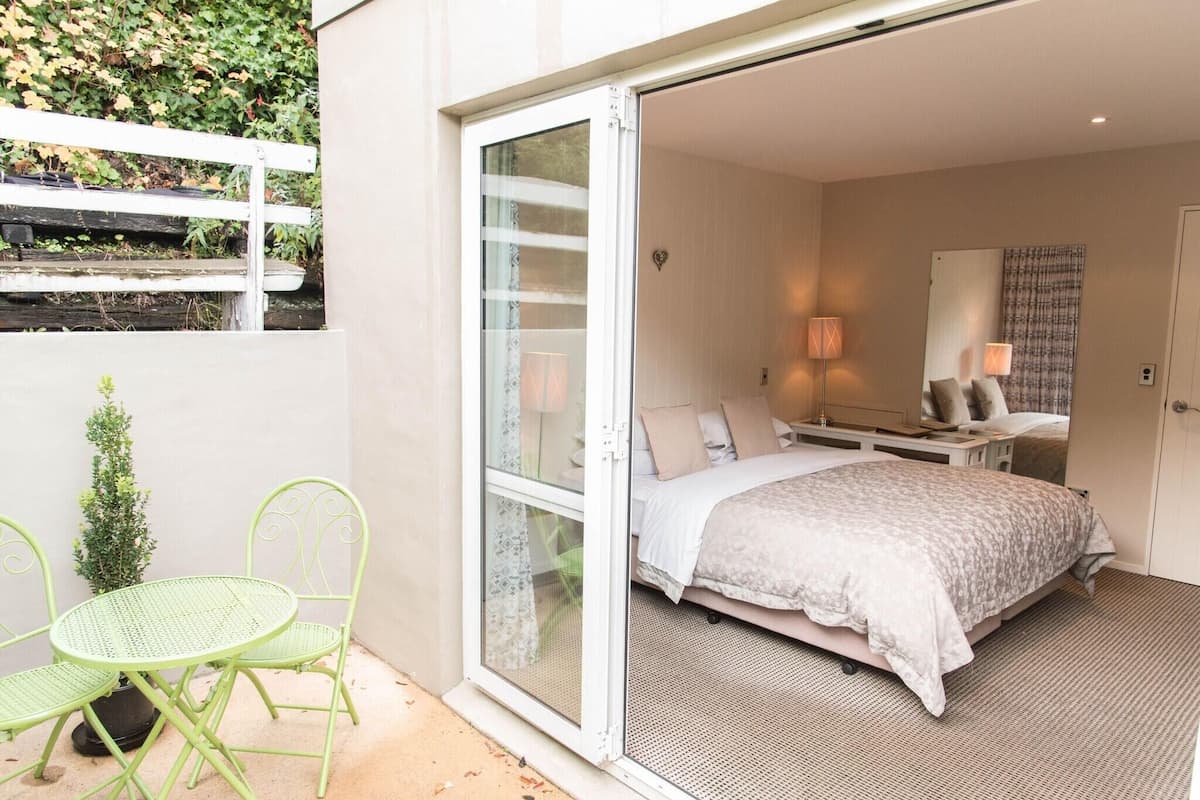 Une chambre à coucher avec un lit, un bureau et une chaise. Il y a une petite table et une plante en pot à l’extérieur de la pièce.