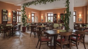 Un restaurante espacioso con numerosas mesas y sillas, iluminación cálida y estanterías a lo largo de las paredes.
