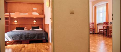 Habitación de hotel con literas, escritorio y sillas. Se ven dos interruptores de luz en la pared y una ventana con cortinas.