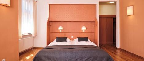 Ein Hotelzimmer mit einem großen Bett, zwei Nachttischlampen, einem Holzkopfstück und einem Fenster mit Vorhängen.