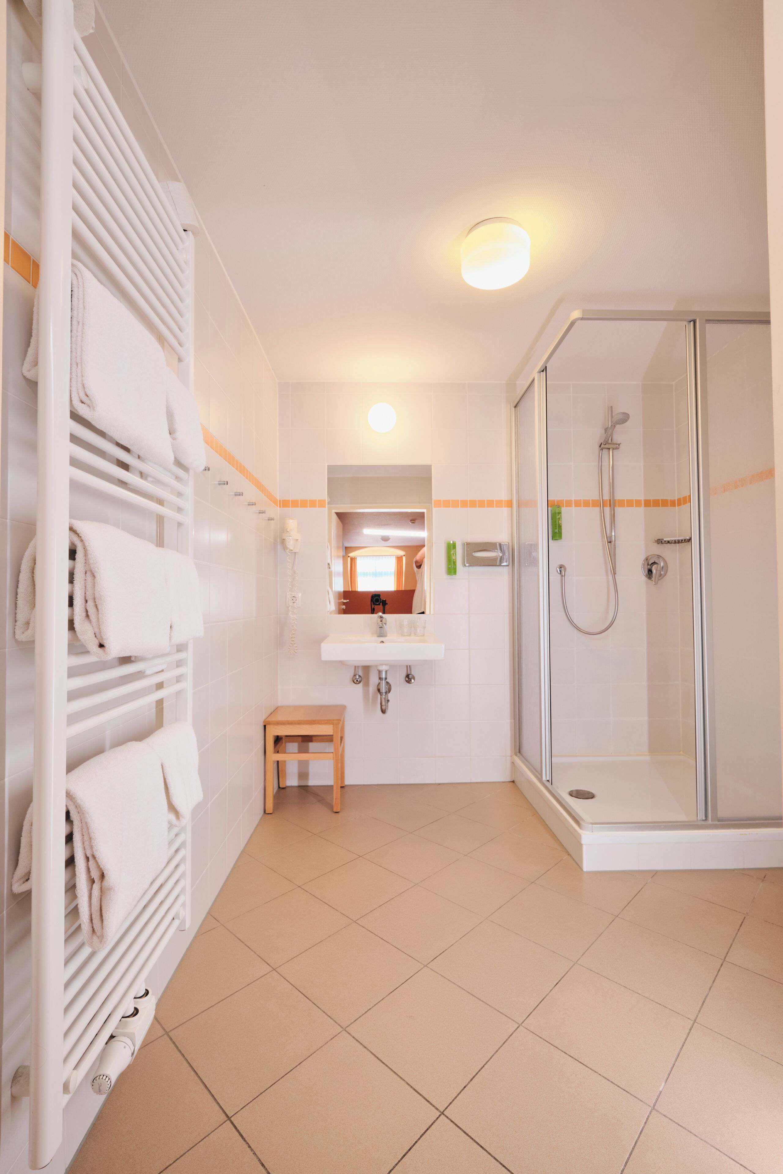 Un baño con cabina de ducha de vidrio, un lavamanos blanco, un espejo sobre el lavamanos y un perchero con toallas dobladas.