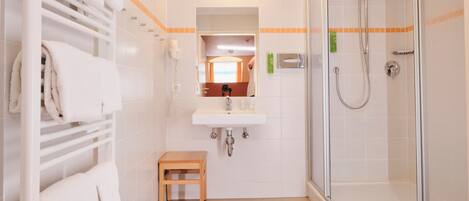 A bathroom with a glass shower enclosure, a white sink, a mirror above the sink, and a towel rack with folded towels.
