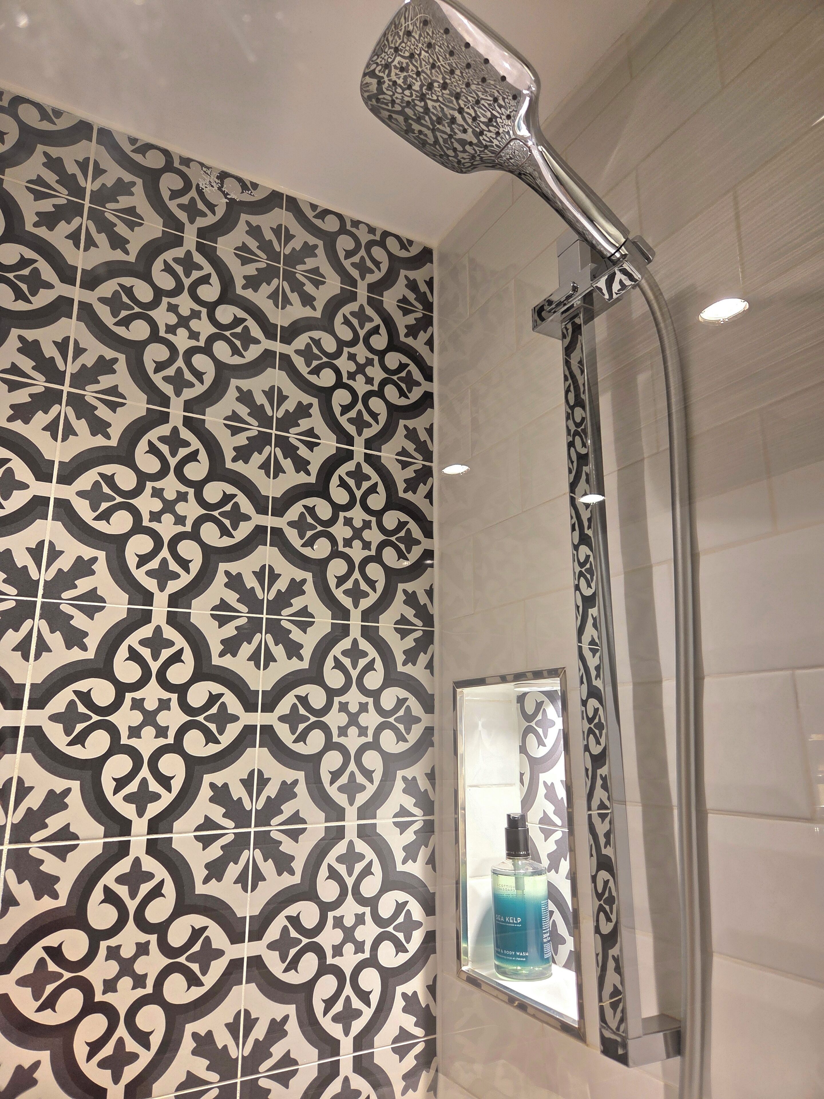 A bathroom with patterned tiles, a showerhead, and a bottle of Sea Kelp body wash on a shelf.