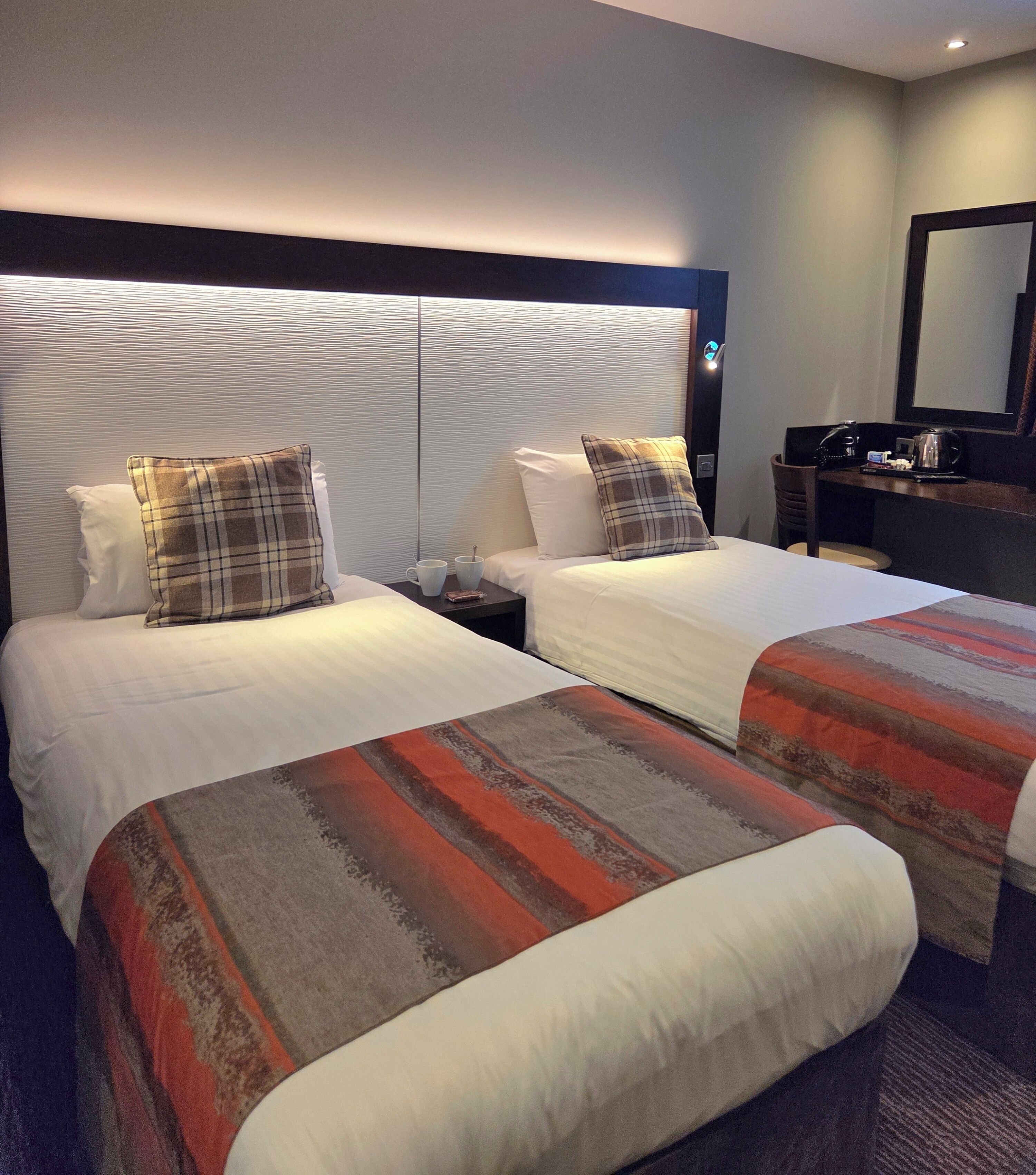 Et hotelværelse med to senge, et natbord, et skrivebord og et spejl.
