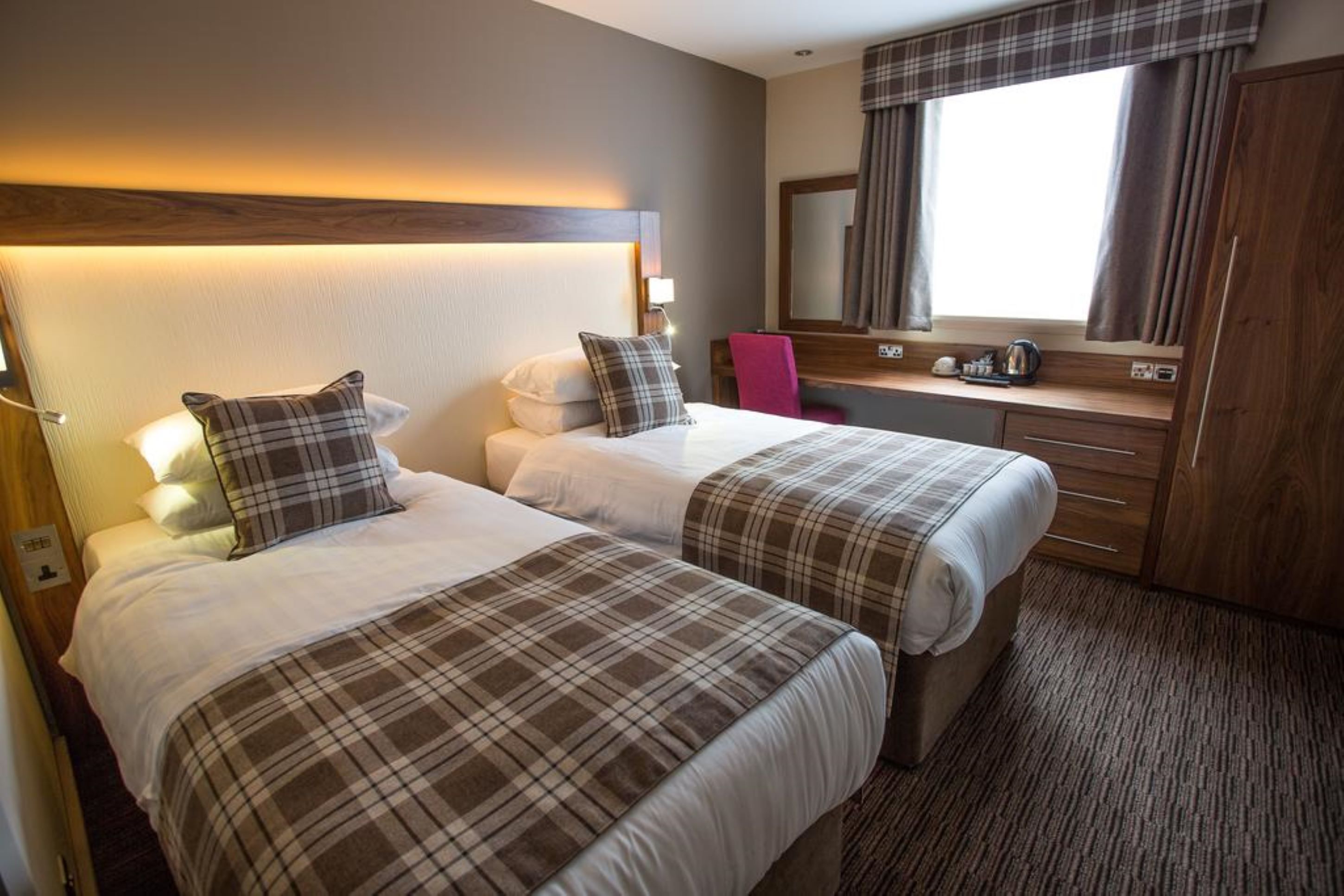 A hotel room with two beds, a desk, a chair, a mirror, and a wardrobe.