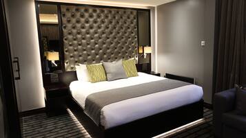 A modern hotel room with a large bed, a tufted headboard, a bedside table with a lamp, and a patterned carpet.