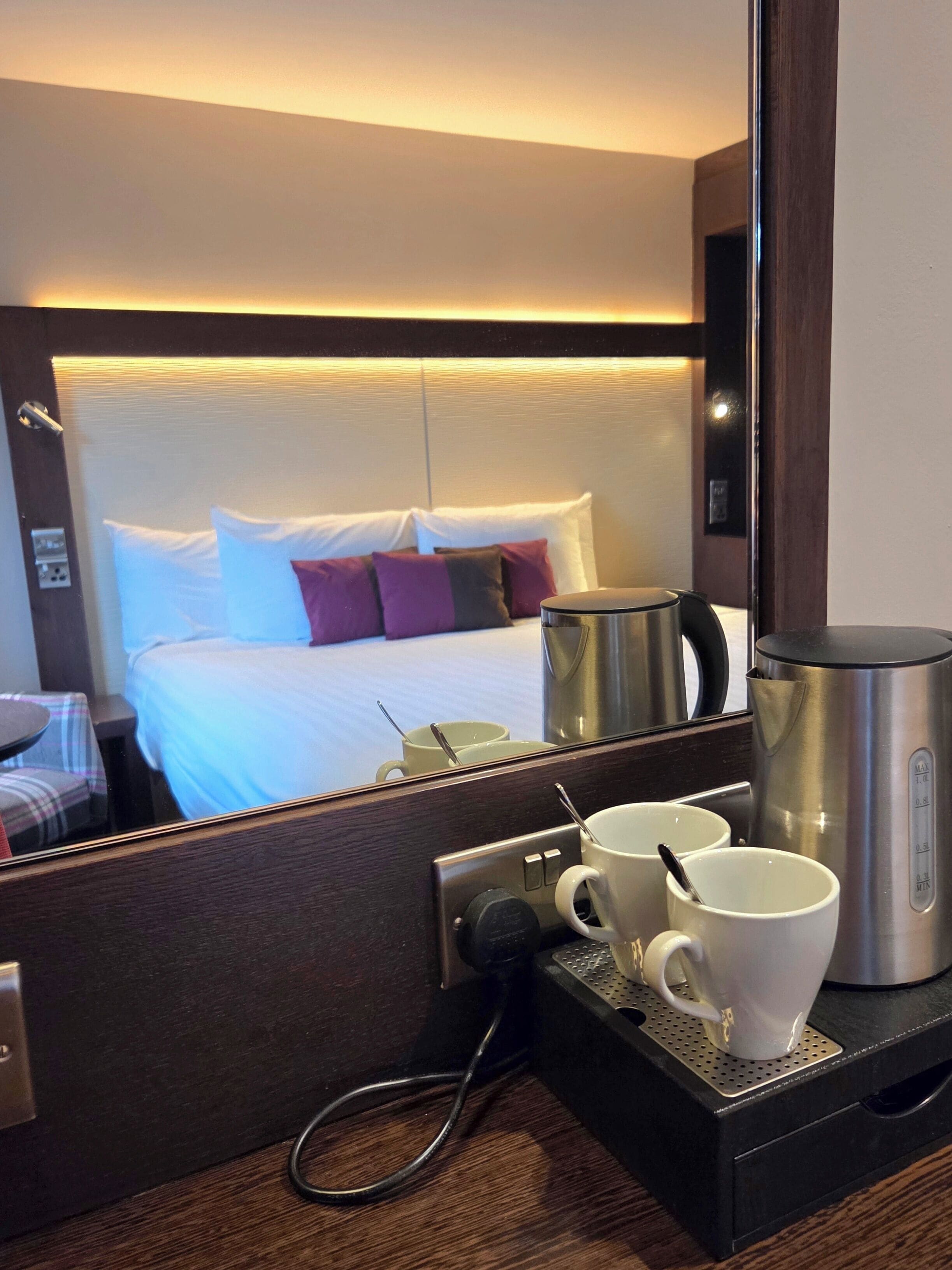Ein Hotelzimmer mit einem Bett, Kissen, einer Kaffeemaschine und einer Tasse auf einem Tablett.