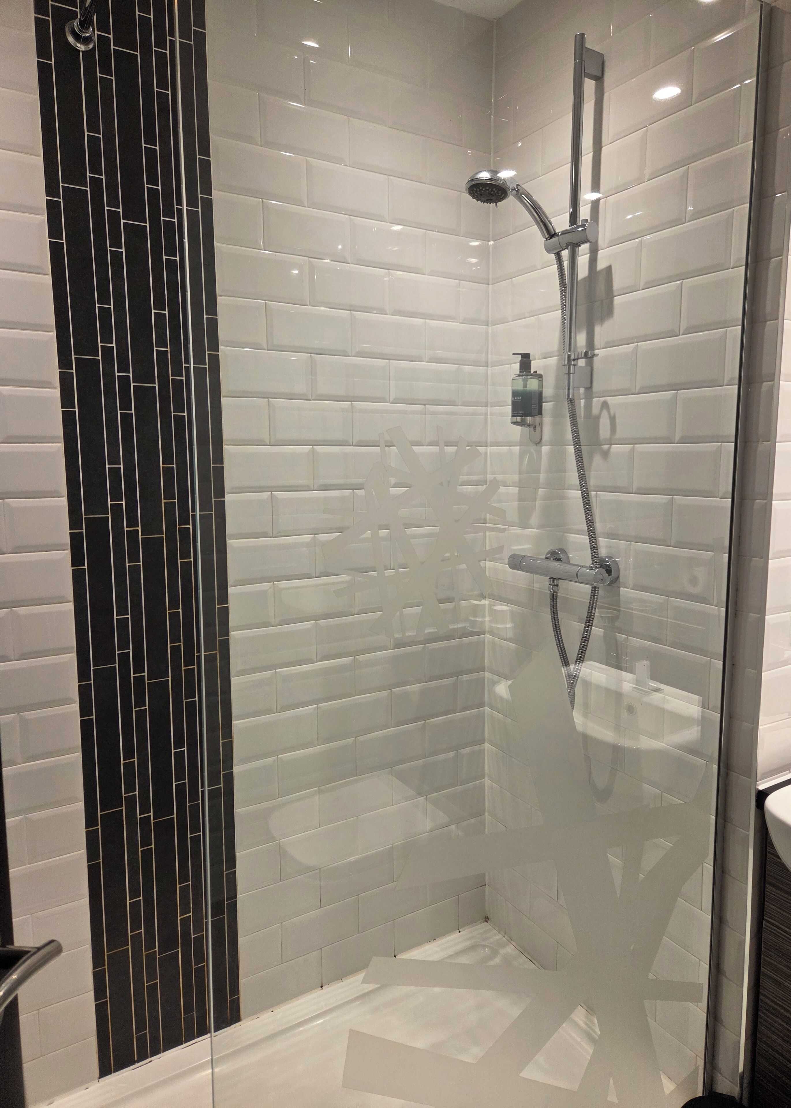 Een moderne douche met een glazen deur, witte betegelde wanden en een zwarte verticale tegel accent.