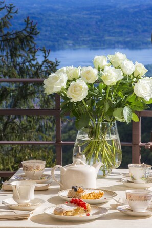 Una mesa dispuesta para el té, con rosas blancas en una jarrón, tetera, tazas, platillos y pasteles.