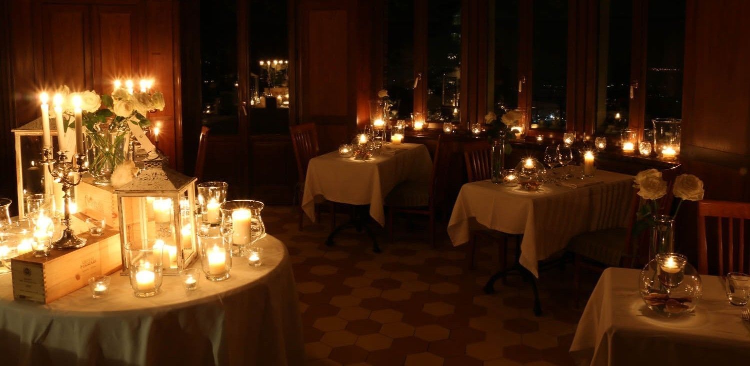Un restaurante tenuemente iluminado con varias mesas dispuestas para cenar, cada una decorada con velas y copas.
