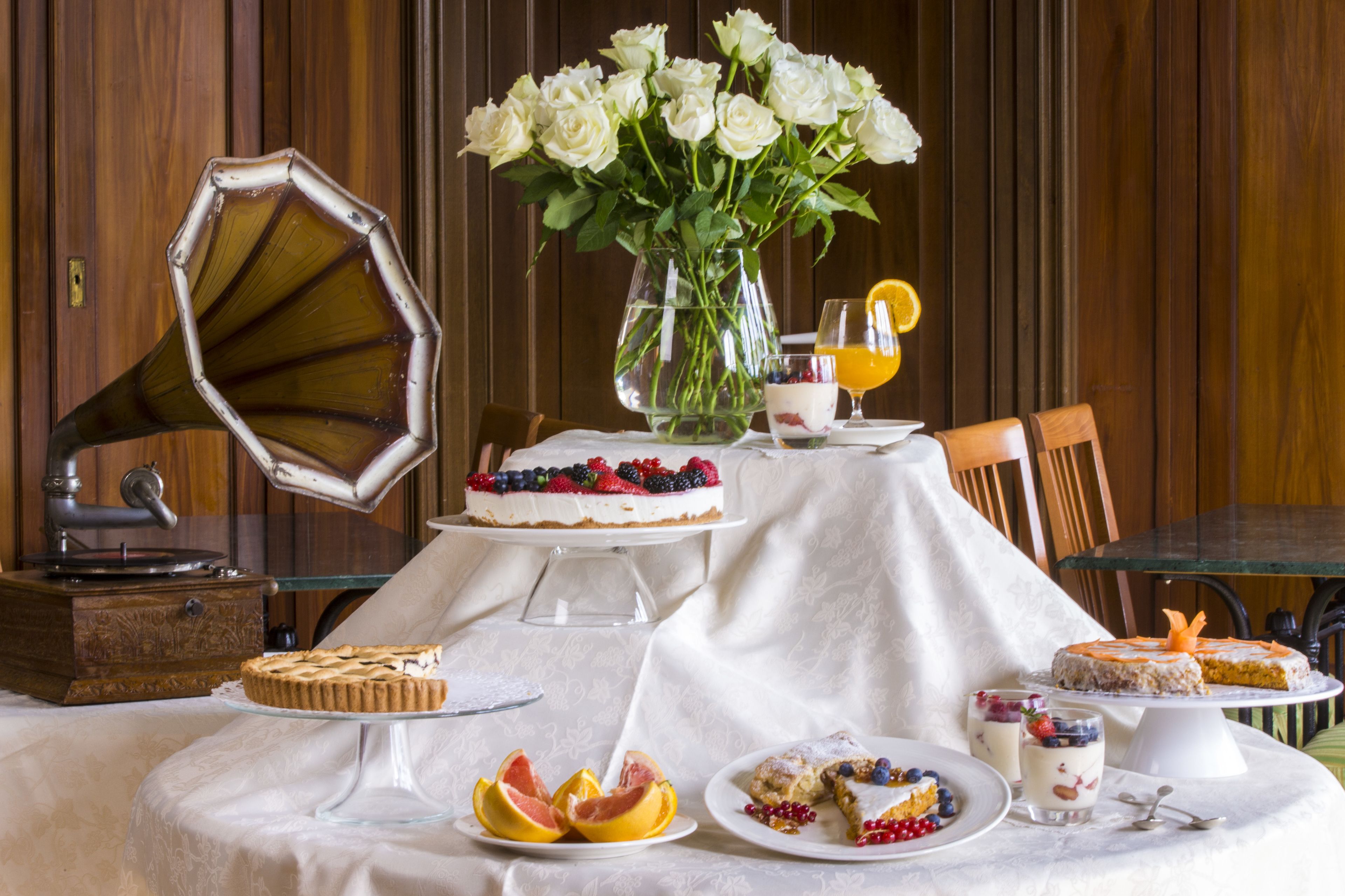 Ein Esstisch mit verschiedenen Desserts, einem Grammophon und einer Vase weißer Rosen.