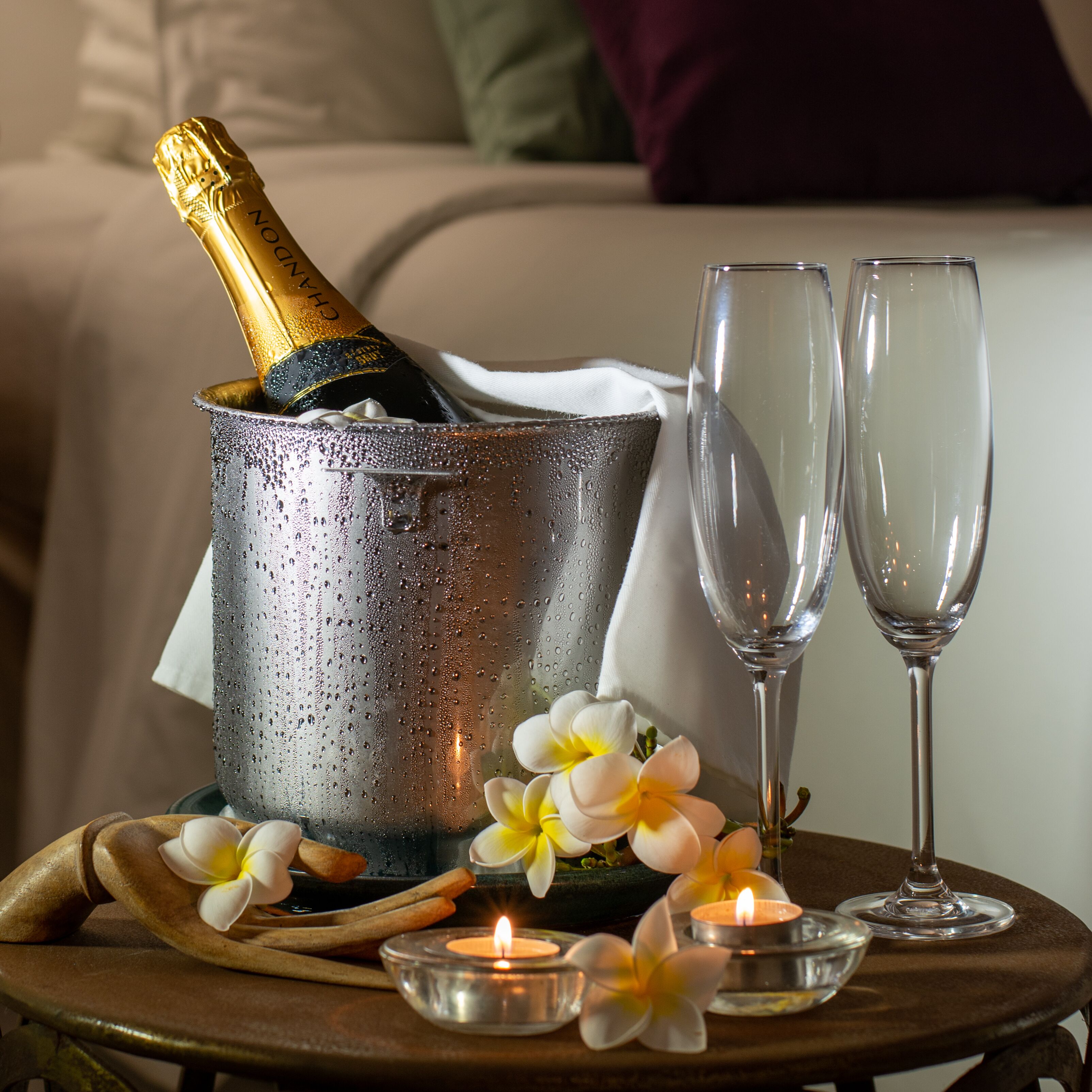 En champagneflaske i et spand, to glas og et lys på et bord med blomster.