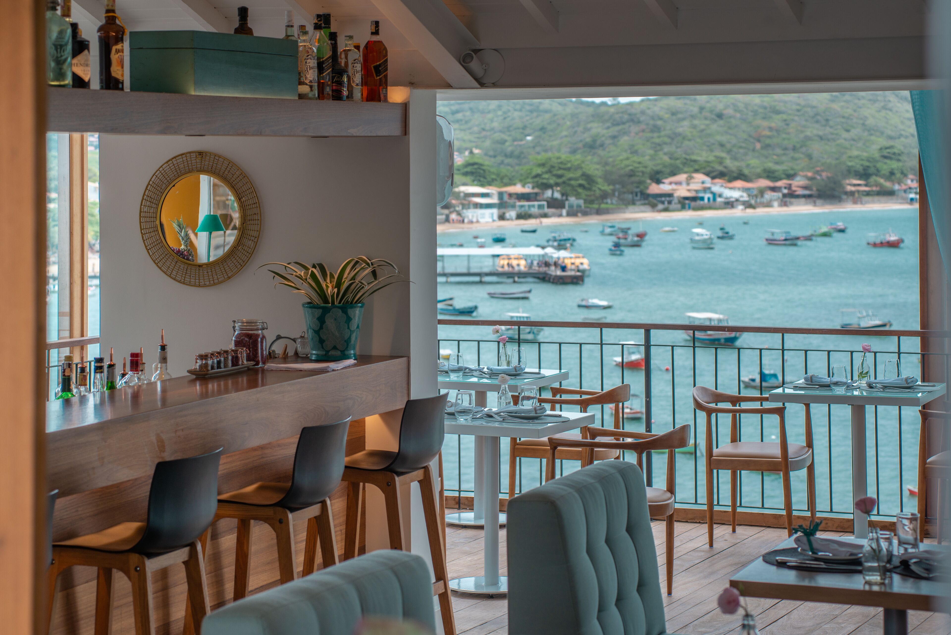 Un restaurante con vistas a barcos en el agua, sillas de madera, una zona de bar con botellas y un espejo en la pared.