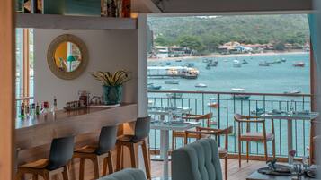 Un restaurante con vistas a barcos en el agua, sillas de madera, una zona de bar con botellas y un espejo en la pared.
