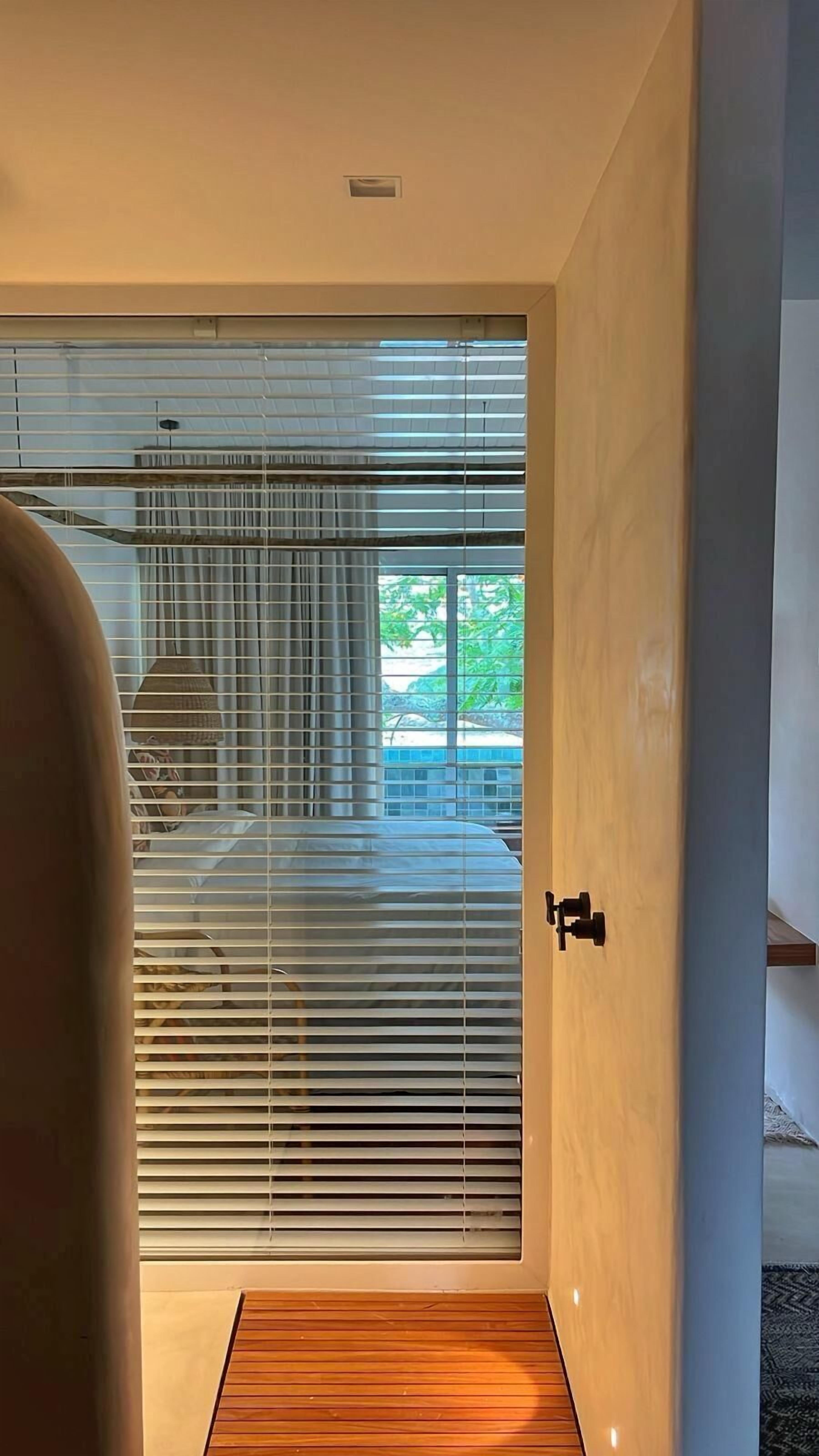 Une chambre moderne avec une grande fenêtre, un plancher en bois et une porte dotée d’une poignée noire.