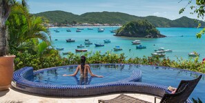 A woman in a swimming pool with a view of boats on a turquoise sea and a green island. - Vila d'este Hotel (Búzios)