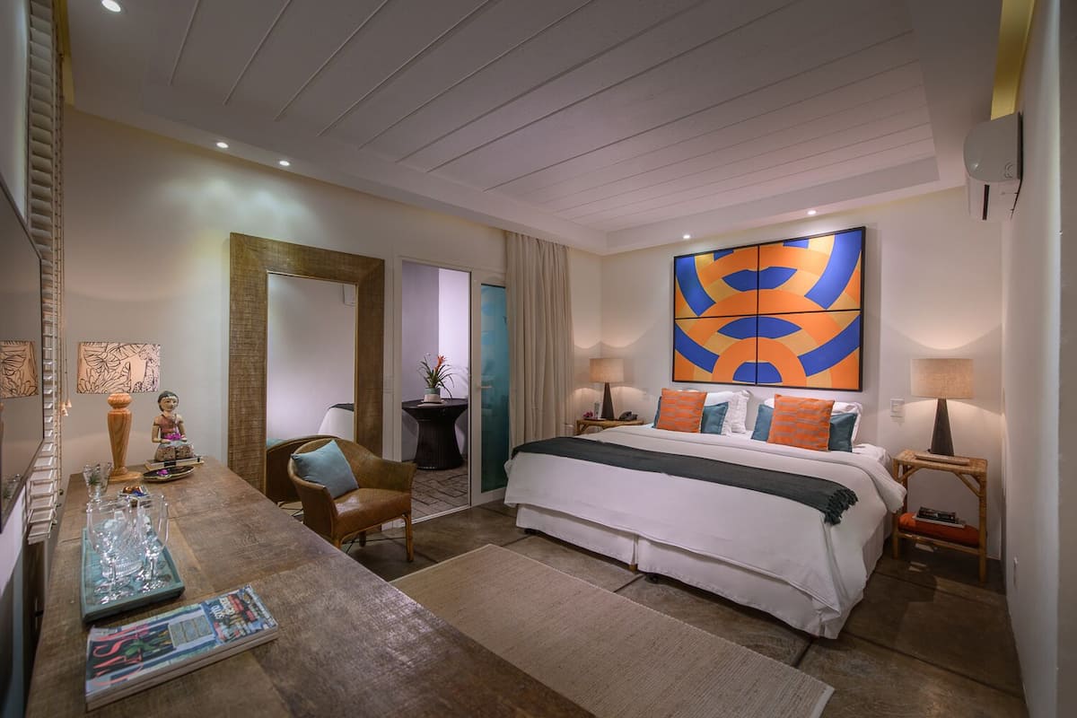 A hotel room with a large bed, a desk with a chair, a mirror, and a wall-mounted TV.