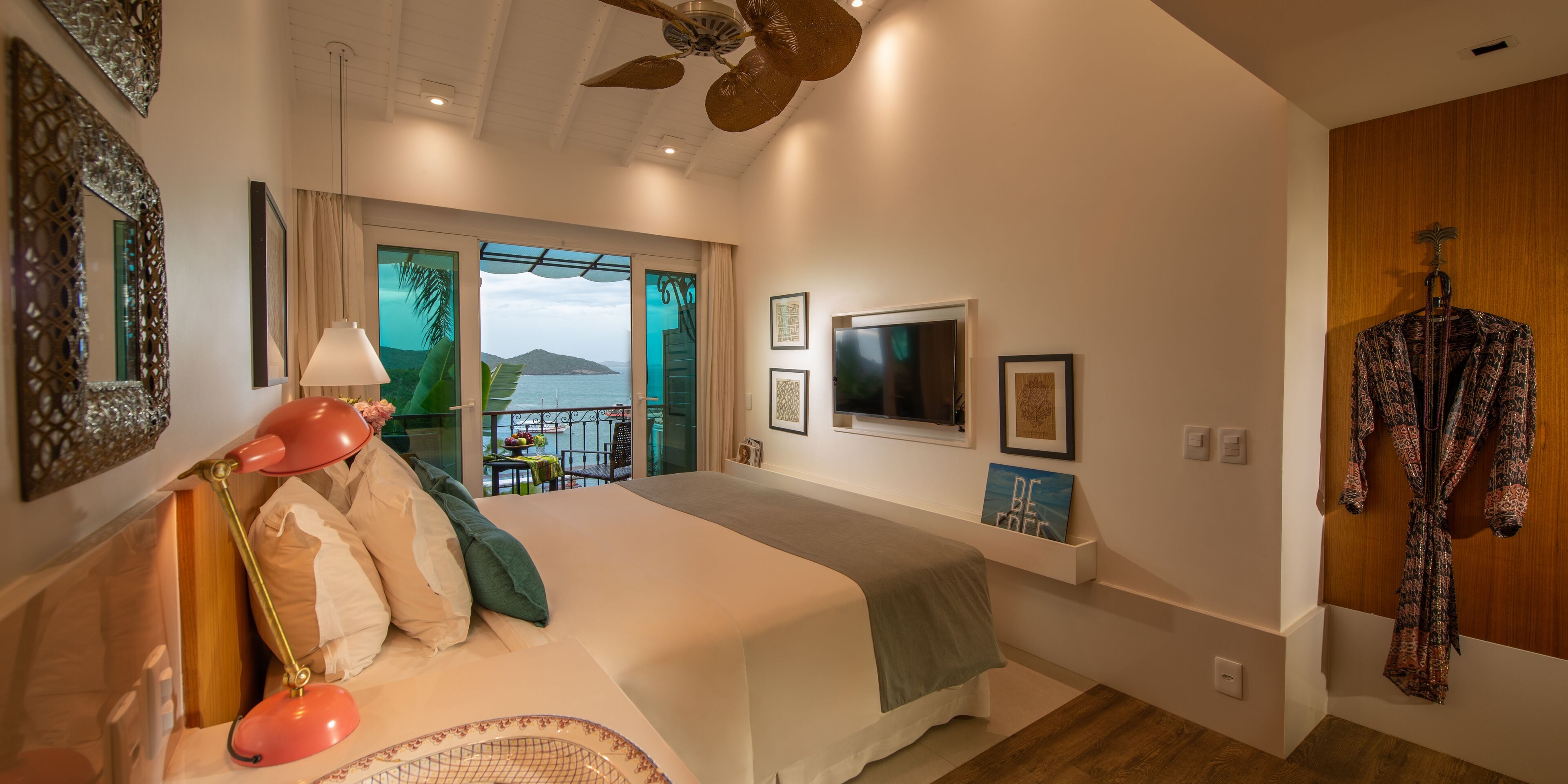 A bedroom with a bed, a ceiling fan, a window with a view, and a robe hanging on the wall.