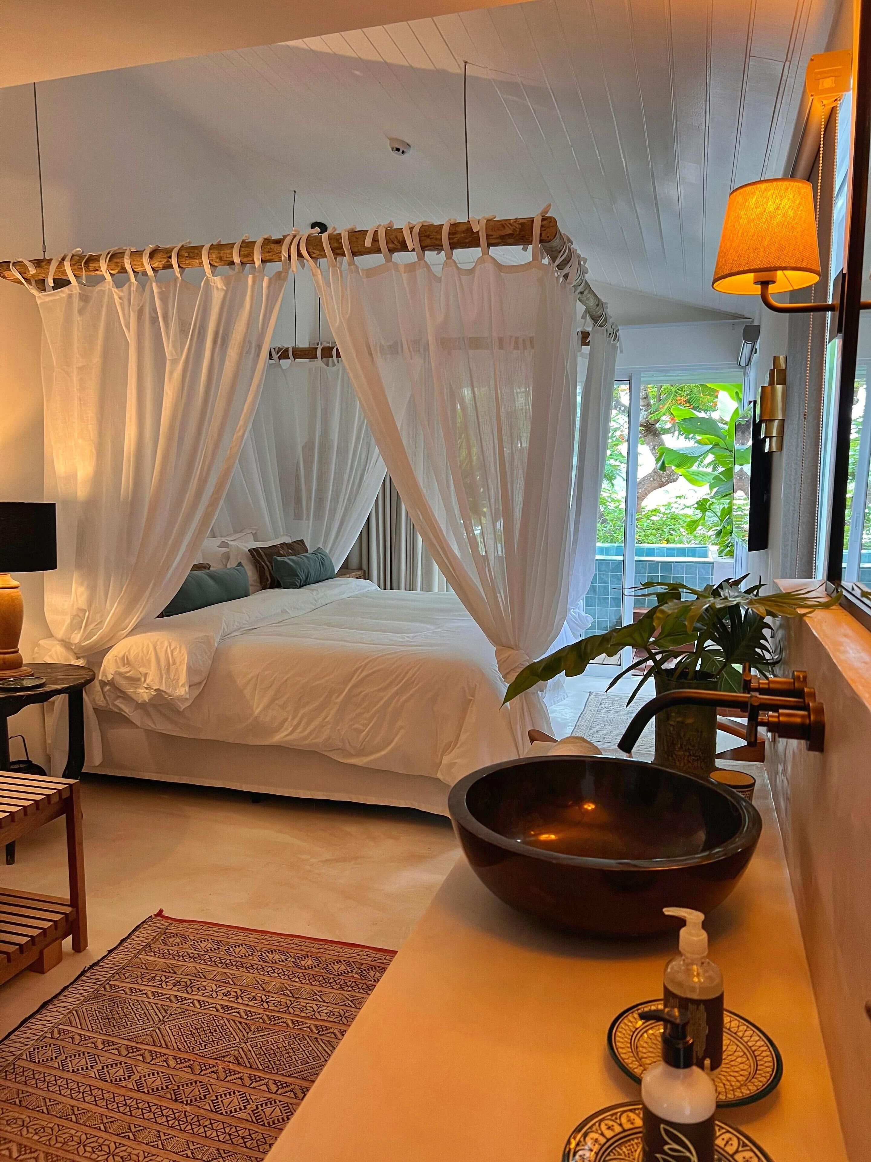 A bedroom with a bed, a bedside table, a lamp, a bowl, and a potted plant.