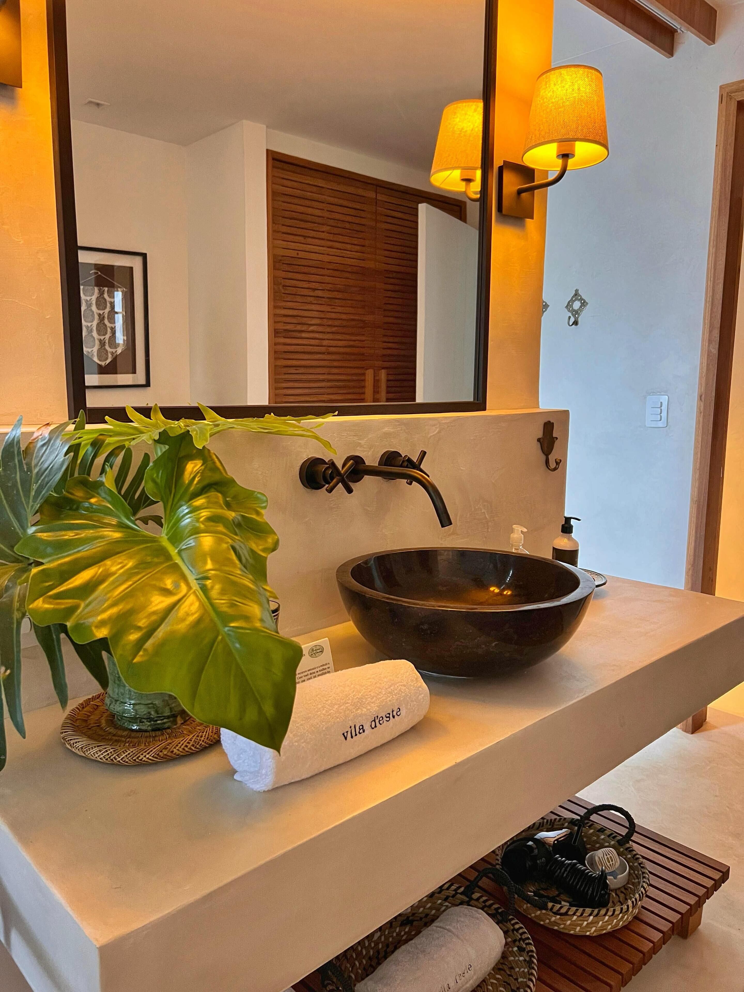 A modern bathroom with a large mirror, a bowl sink, a potted plant, and a towel rack.