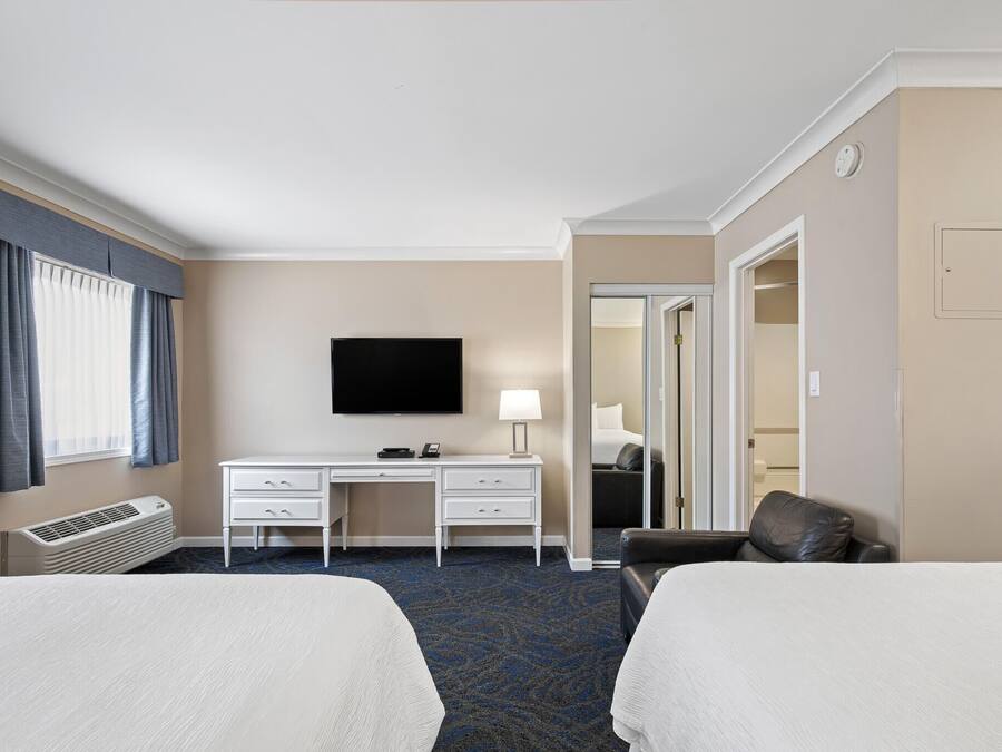 A hotel room with two beds, a desk, a TV, and a chair.