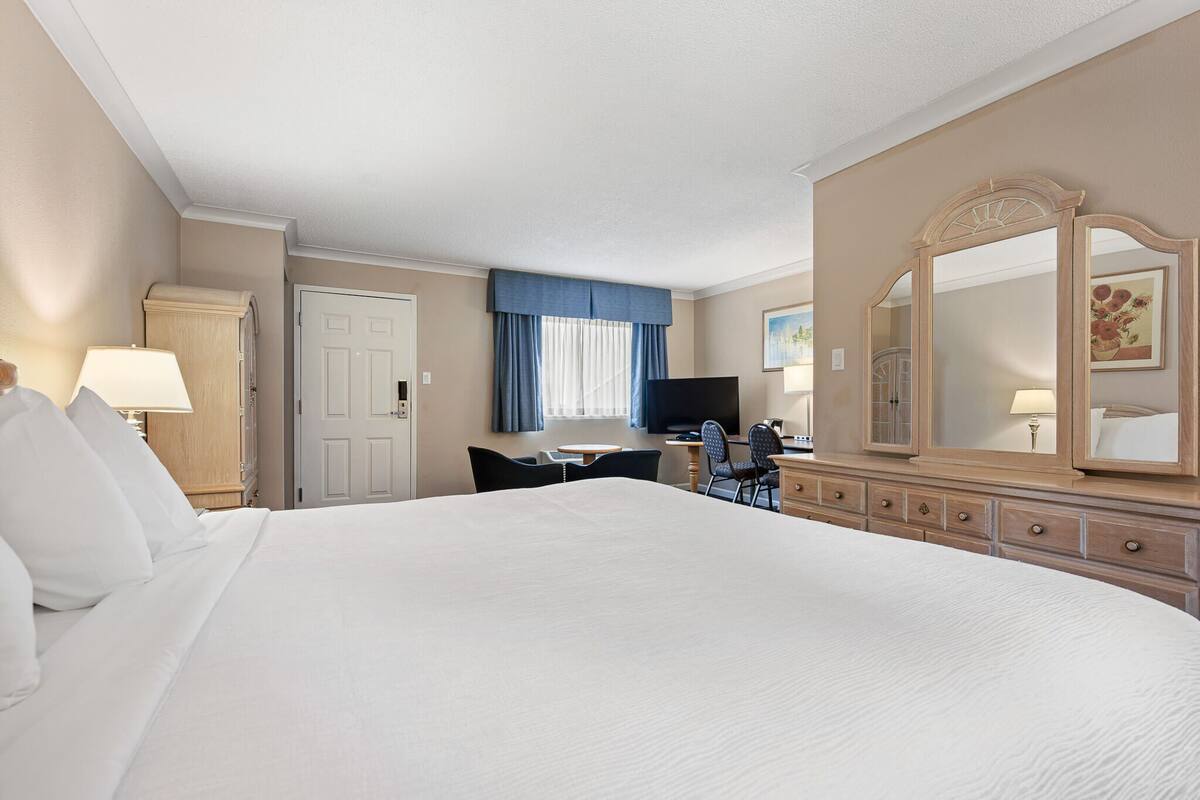 Ett hotellrum med en stor säng, ett skrivbord med en stol, en tv, en byrå och en spegel.