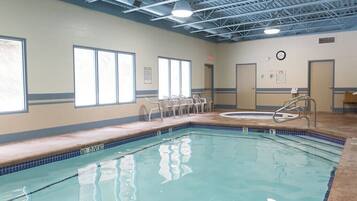 An indoor swimming pool with clear water, a diving board, and a clock on the wall.