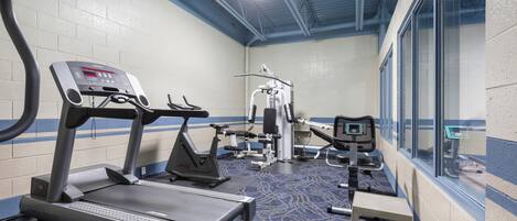 Ein Fitnessstudio mit Laufbändern, Kraftgeräten und einem blau teppichbedeckten Boden.