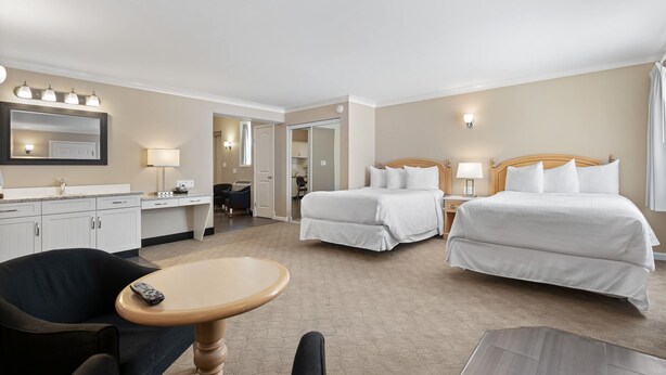 A hotel room with two beds, a desk, a chair, a table, and a mirror. - Glenwood Inn & Suites (Trail)