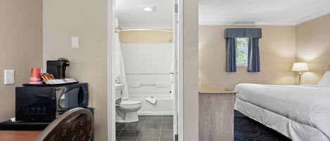 Hotelkamer met een bed, een bureau met een magnetron, een stoel, een badkamer met toilet en wastafel, en een raam met gordijnen.