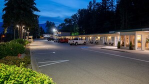 A motel with a row of rooms, a parking area, and a building with a lighted entrance. - Glenwood Inn & Suites (Trail)