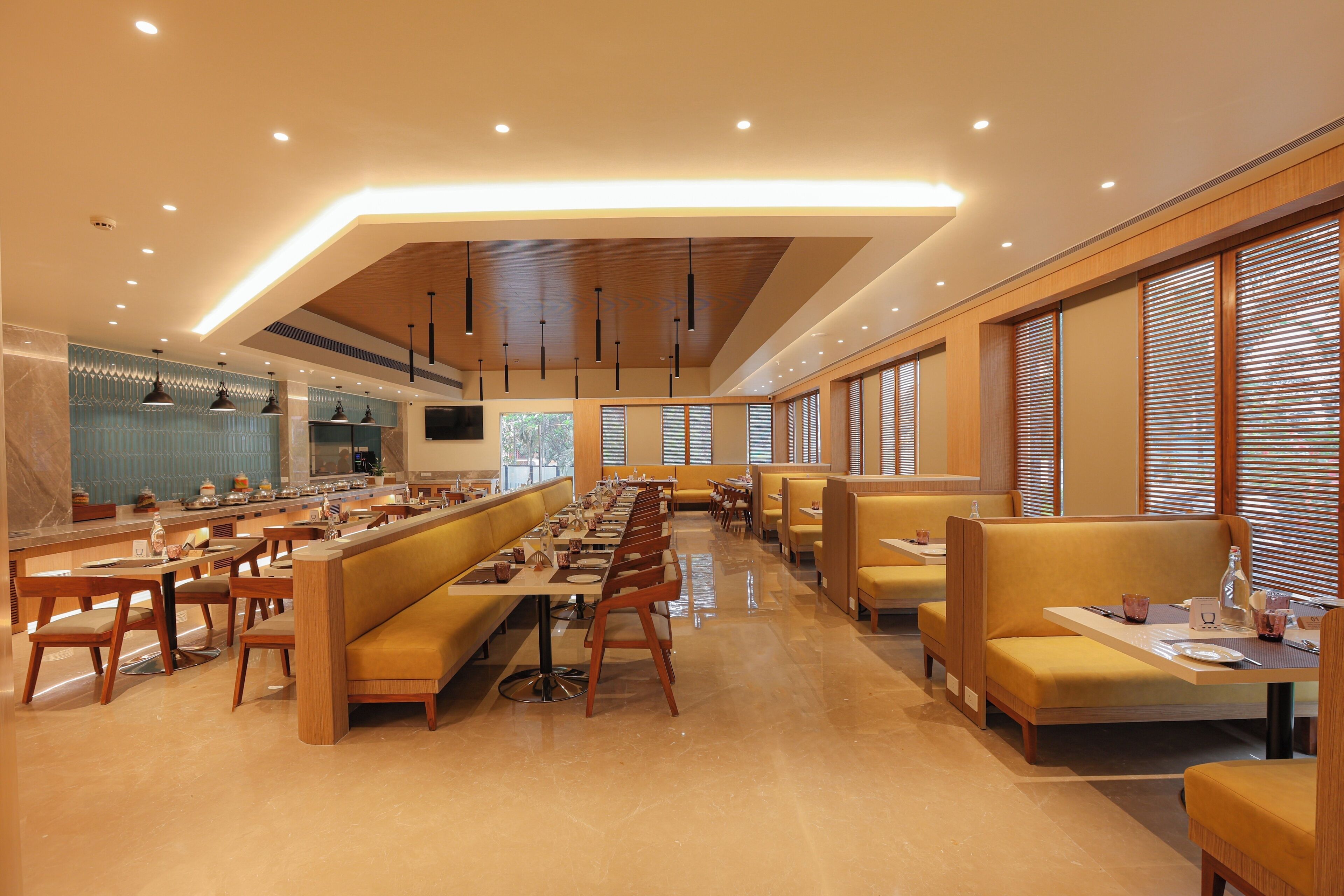 A spacious restaurant with long communal tables and booths, wooden flooring, and large windows with blinds.