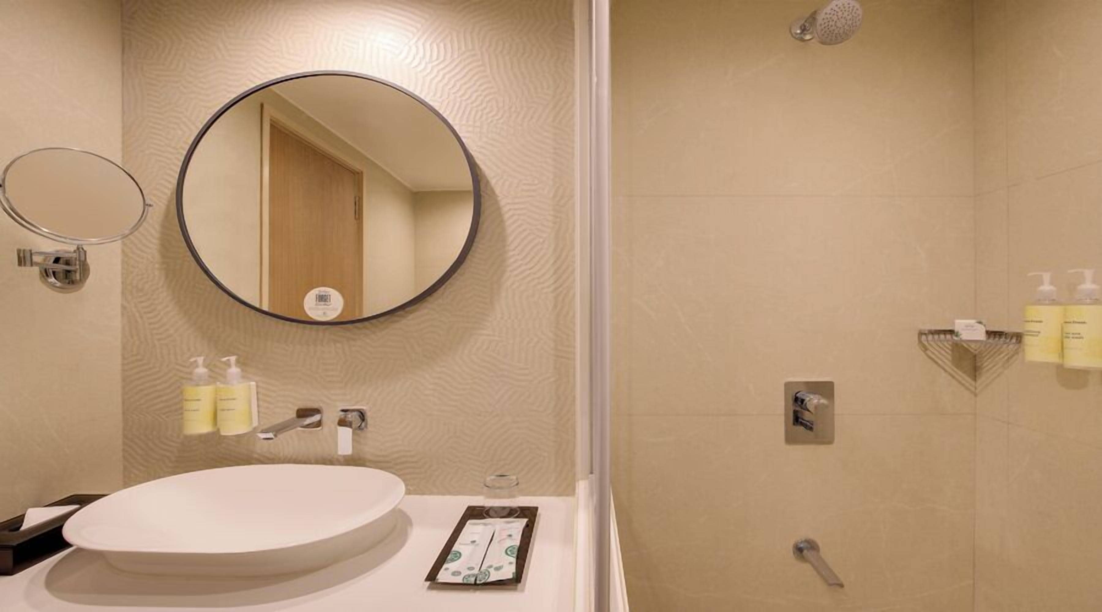 A bathroom with a round mirror, a sink, and a shower area.