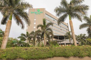 A hotel with a modern design, palm trees, and a well-maintained garden.