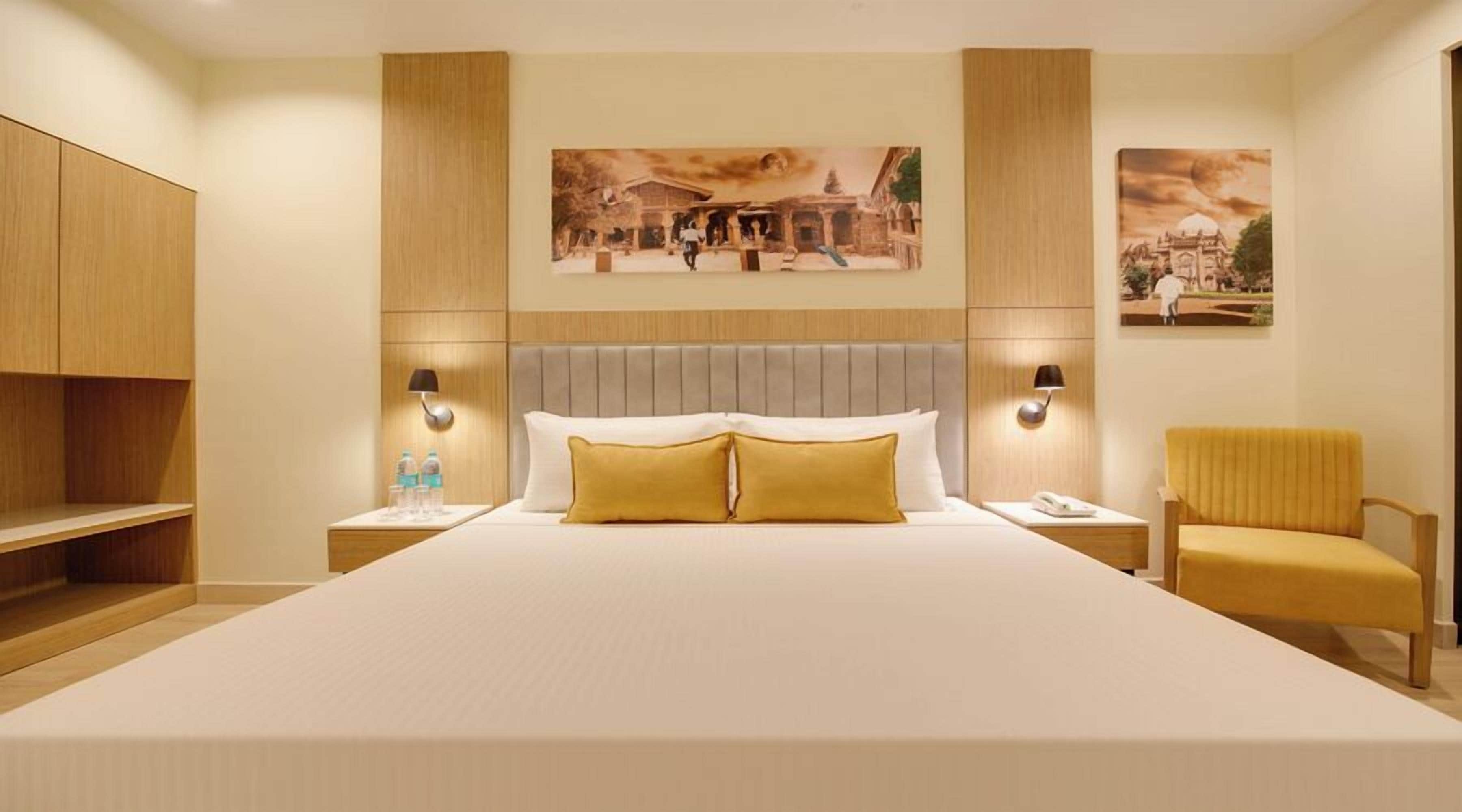 Un letto grande con testiera, due comodini con lampade, una sedia e opere d'arte alle pareti.