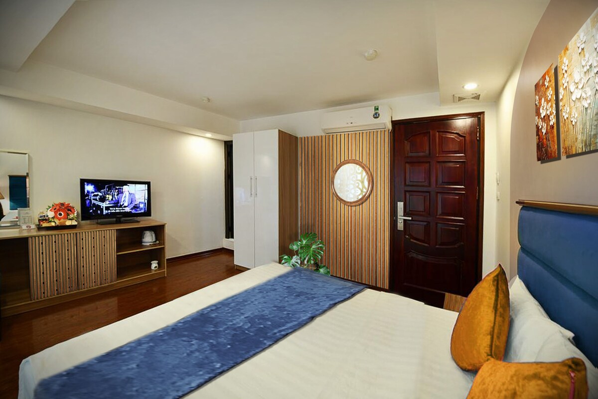 Ein Hotelzimmer mit Bett, Fernseher auf einer Holzkonsole, einer Tür mit rundem Spiegel und einem Bild an der Wand.