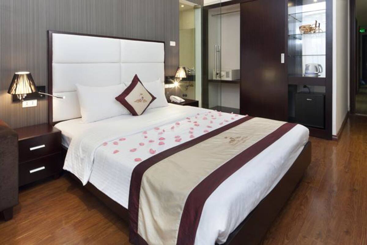 A hotel room with a large bed, a nightstand, a chair, and a wardrobe.
