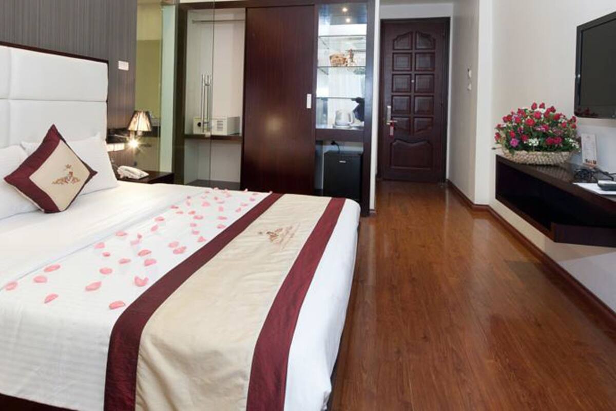 A hotel room with a large bed, a wooden floor, a TV, and a door leading to a bathroom.