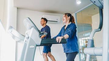 Two people using treadmills in a gym with a large window and an air conditioning unit on the wall.