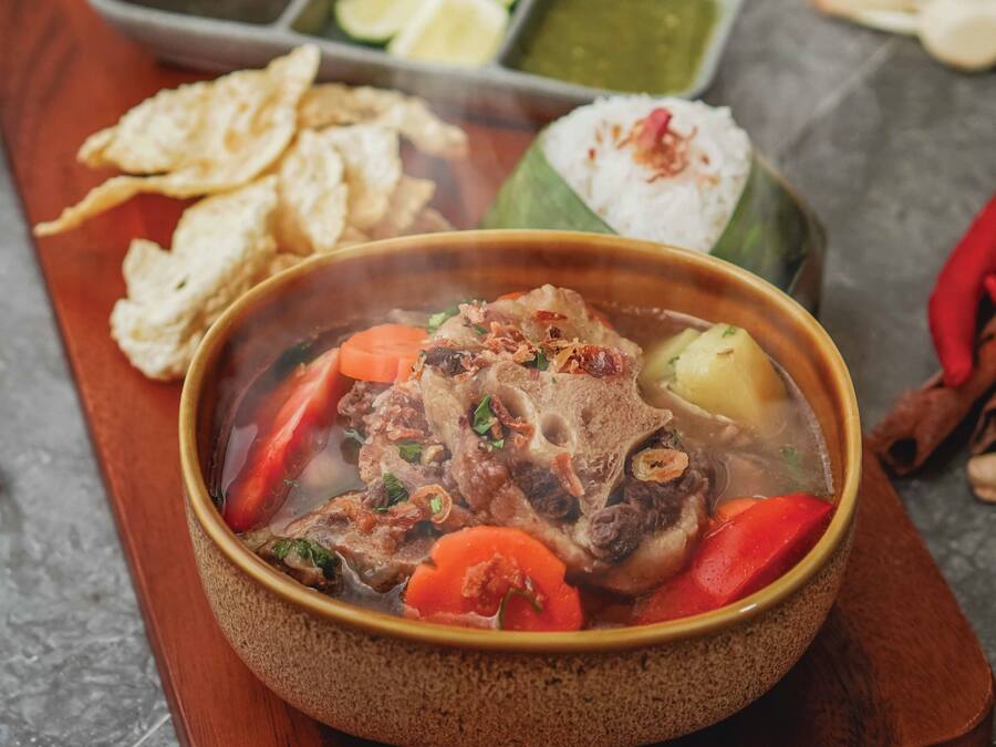 Un tazón de sopa con carne y vegetales, acompañado de arroz, papas fritas y salsas.