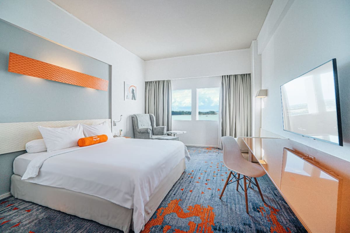 Ein Hotelzimmer mit Bett, Schreibtisch, Stuhl, Fernseher und einem Fenster mit Vorhängen.